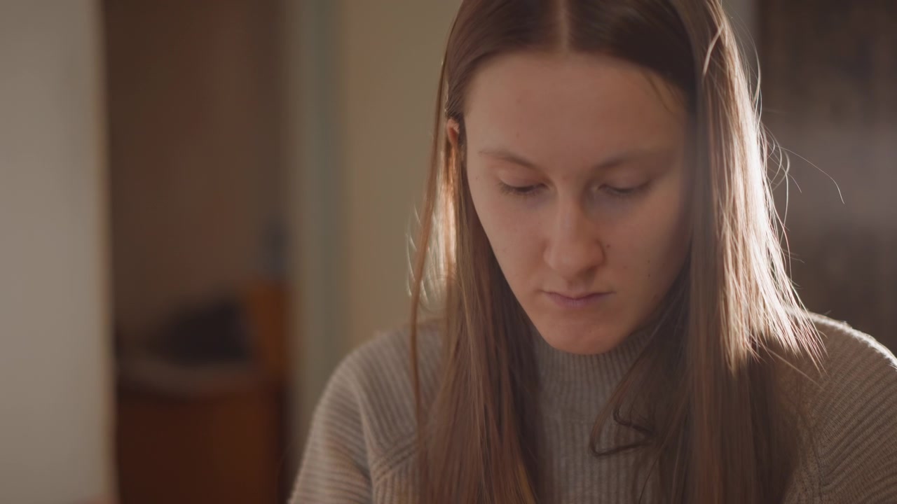 Caucasian woman by window studying. Serene woman immersed in study with warm lighting ambiance at home. Tranquil Caucasian female engaged in reading near window with soft cinematic illumination