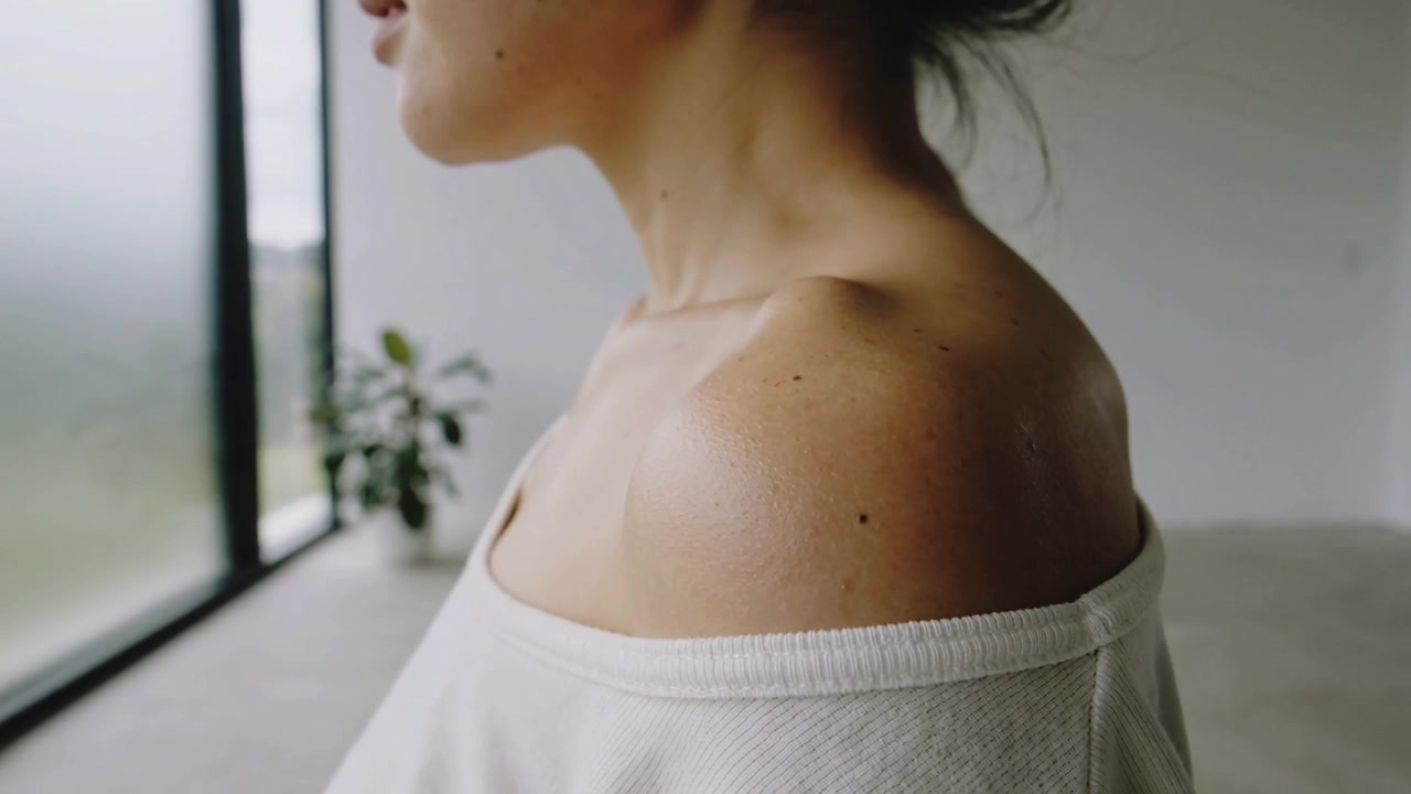 Reagendo alla luce della finestra, una donna sposta la spalla in avanti vicino alla finestra, indossando un top a spalle scoperte.