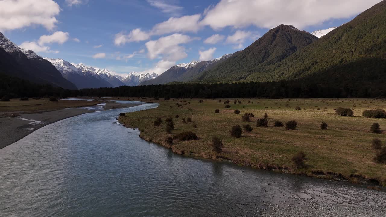 Ripresa cinematografica a bassa quota con drone di un limpido torrente di montagna che scorre tra cime innevate nel Southland, Nuova Zelanda, in direzione di Milford Sound a 4K 60 fps