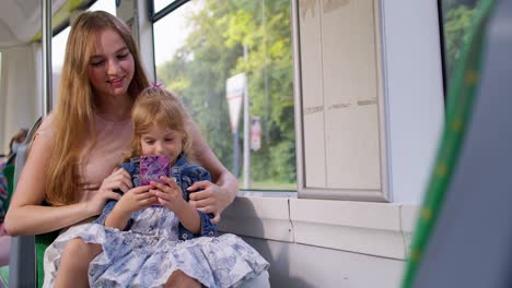 Mother-with-daughter-traveling-by-bus-going-home,-playing-on-smartphone,-browsing-social-media