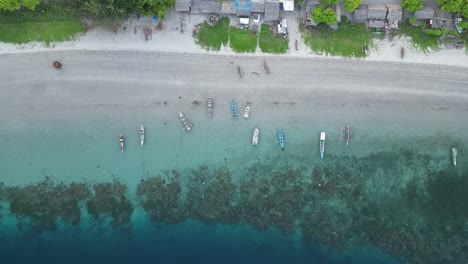 boats anchored along a coral-filled coastline with clear blue waters from an aerial view