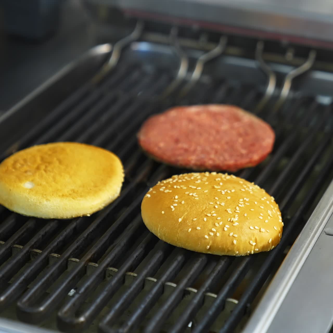 Two buns are grilled on a barbeque grid. Raw cutlet being fried on grill. Unhealthy tasty dish