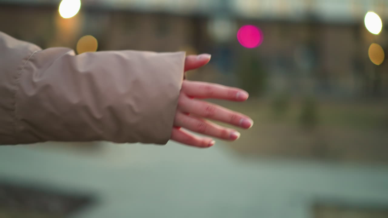 부드러운 조명과 보케 효과를 특징으로하는 흐릿한 도시 배경 앞에 펼쳐진 사람의 손의 클로즈업. 복아 재을 입은 손이 주요 초점입니다.