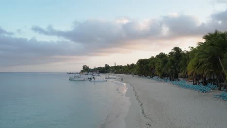 White-Boats-on-the-waves-in-azure-seawater,-palms-and-resorts-on-Caribbean-coast