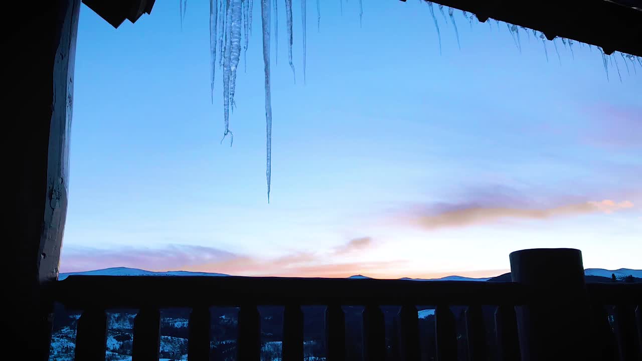 Winter sunrise over mountain range time lapse from balcony with icicles