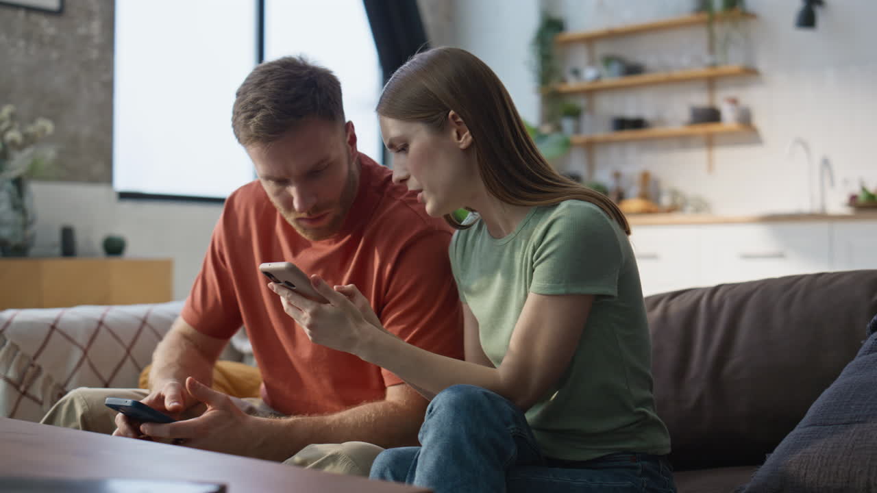 Serious couple looking cellphone sitting together at sofa living room closeup