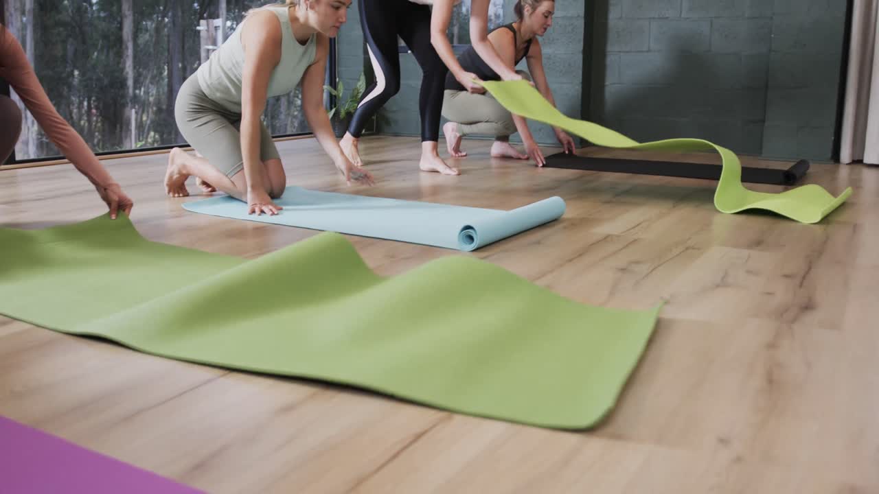 mujeres diversas se centraron en desplegar esteras en el suelo en la clase de yoga con una entrenadora femenina, cámara lenta