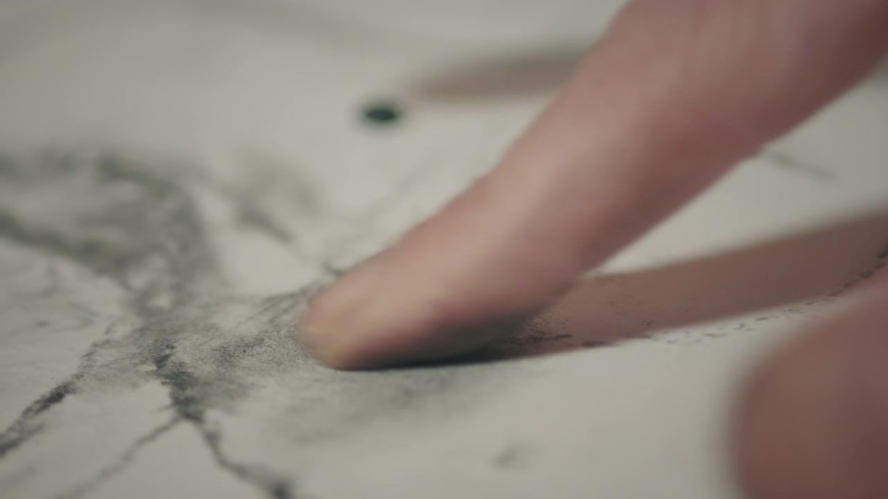 Macro close-up of finger smudging charcoal across paper, emphasizing tactile technique, control, and immersive learning in an evening art class.