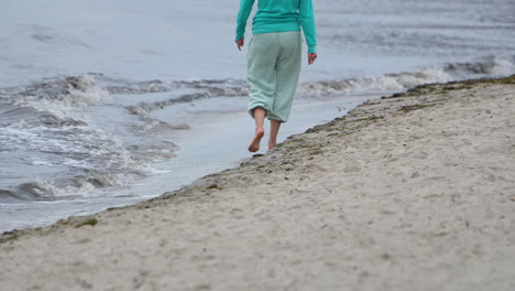 person walking barefoot on the sandy beach, waves lapping at the shore