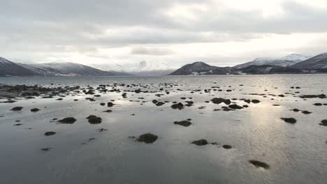 Drone-shot-flying-low-over-a-fjord-in-Norway-with-snow-capped-mountains