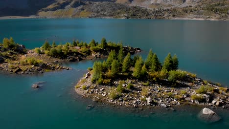 Sobrevuelo-Aéreo-Sobre-Una-Isla-En-Las-Aguas-Del-Lago-De-Salanfe-En-Valais,-Suiza-En-Un-Soleado-Día-De-Otoño-En-Los-Alpes-Suizos-Con-Una-Vista-Panorámica-Desde-Los-Picos-Y-Acantilados-Alpinos-Circundantes