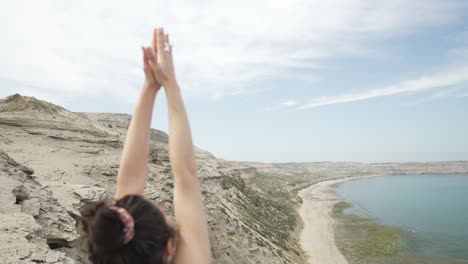 vista de atrás de una mujer joven haciendo yoga de calentamiento en una hermosa ubicación de paisaje oceánico - zoom in