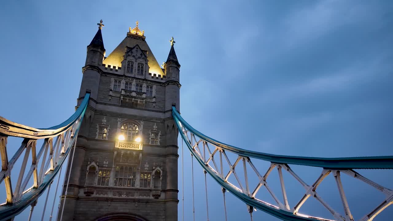 Perspektif nadir berjalan melintasi Jembatan London saat matahari terbenam, menampilkan arsitektur ikonik jembatan, langit dramatis, dan suasana ramai ibu kota Inggris selama golden hour