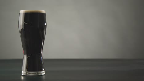 person picking up pint of irish stout in glass against studio background to celebrate st patricks day 2