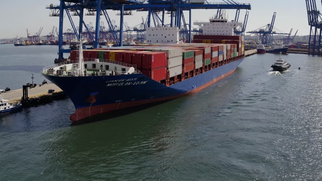 Luftfoto af et fragtskib i en travl havn, der viser farverige containere og kraner