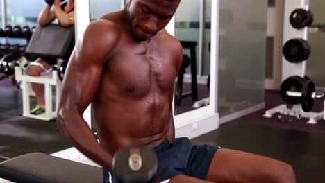 Fit-shirtless-man-lifting-dumbbells-sitting-on-bench