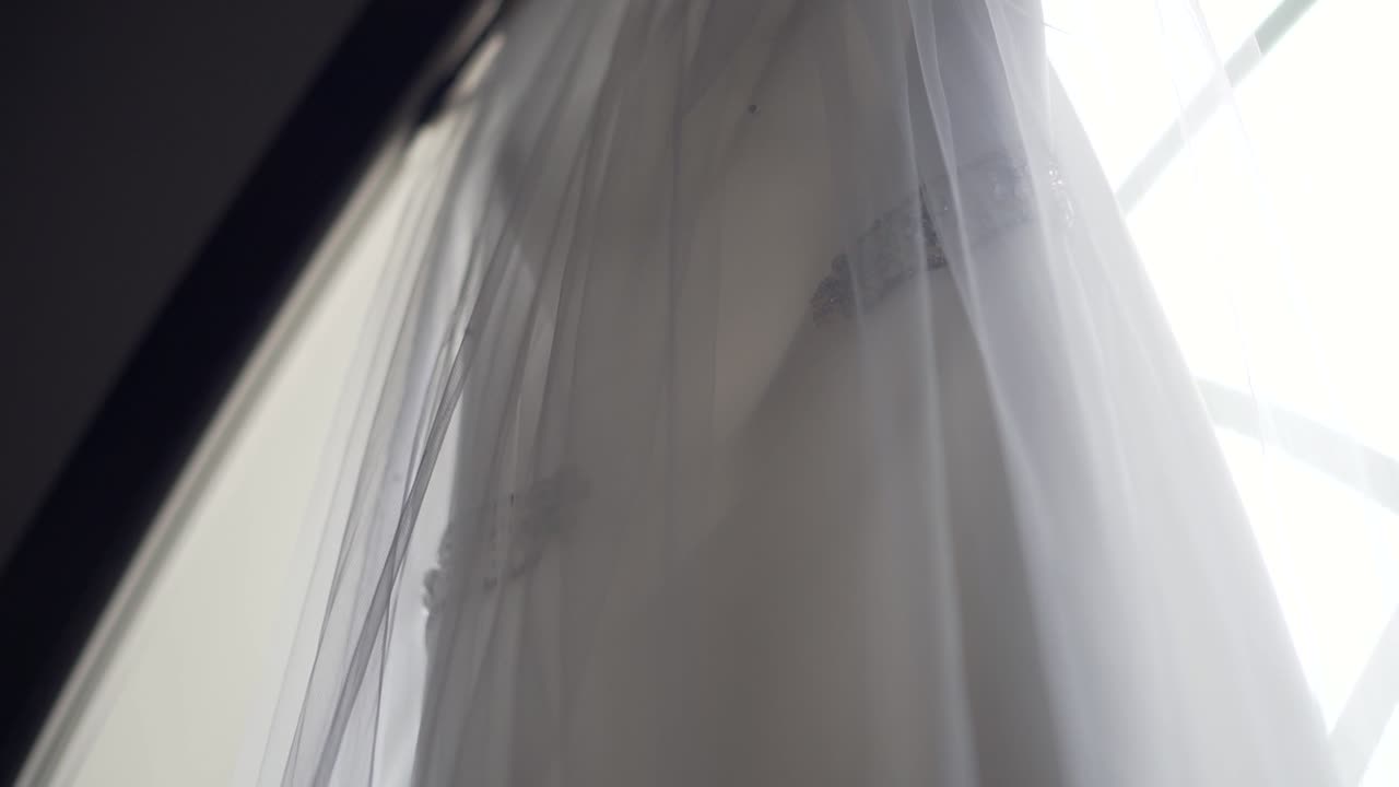 Nahaufnahme eines wunderschönen Hochzeitskleides, das auf einer großen Kirchenfensterbank hängt – Zeitlupe: Schwenk von rechts nach links