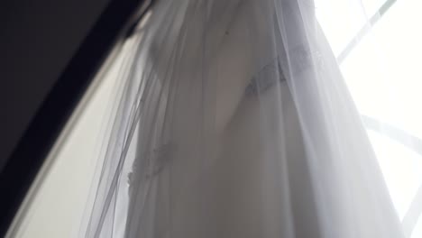 Nahaufnahme-Eines-Wunderschönen-Hochzeitskleides,-Das-Auf-Der-Großen-Kirchenfensterbank-Hängt-–-Zeitlupenschwenk-Von-Rechts-Nach-Links