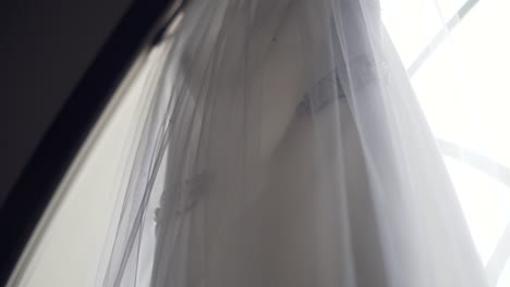 close up shot of a beautiful wedding dress hanging in large church window sill - slow motion right to left pan