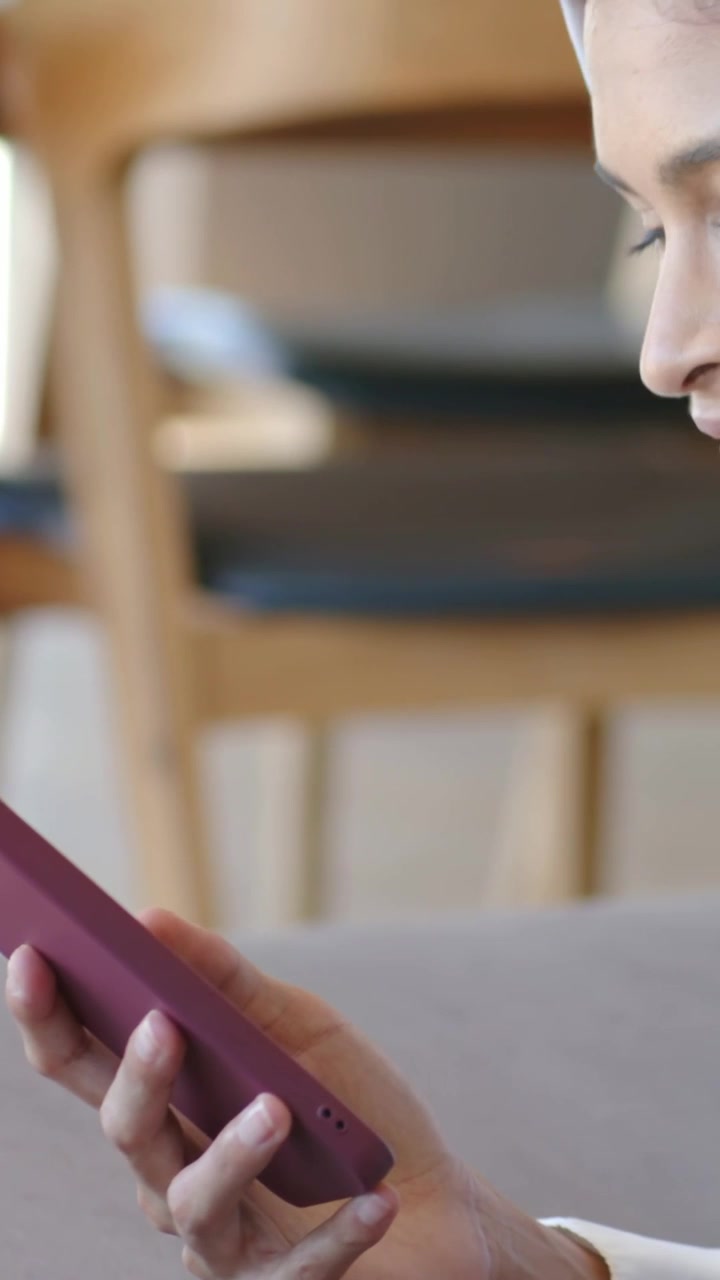 Video verticale: Donna sul divano con una sciarpa che solleva un telefono viola e legge lo schermo, con spazio per il testo.