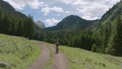 aerial tracking shot of cyclist with mountain bike riding on path between dolomite mountains in summer - beautiful mountain panorama in italy