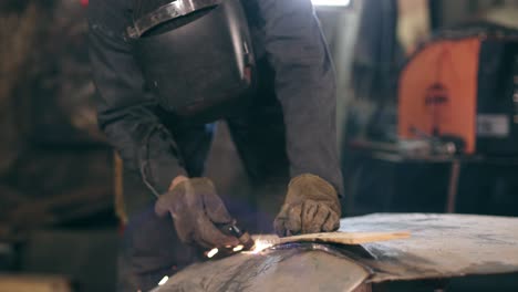 Unrecognizable-worker-with-welding-helmet-on-cuts-off-metal-piece-with-a-oxy-acetylene-cutting-torch-at-a-mechanical-hangar