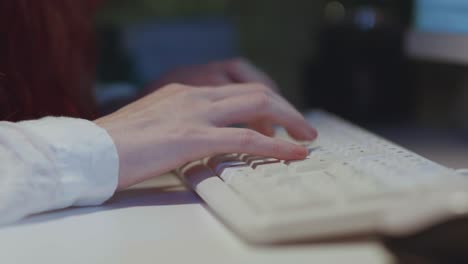 a close-up, side-angle shot of a woman's hands typing quickly on a white computer keyboard in a dimly lit office. this footage is for concepts of work, writing, coding, data entry, and communication.