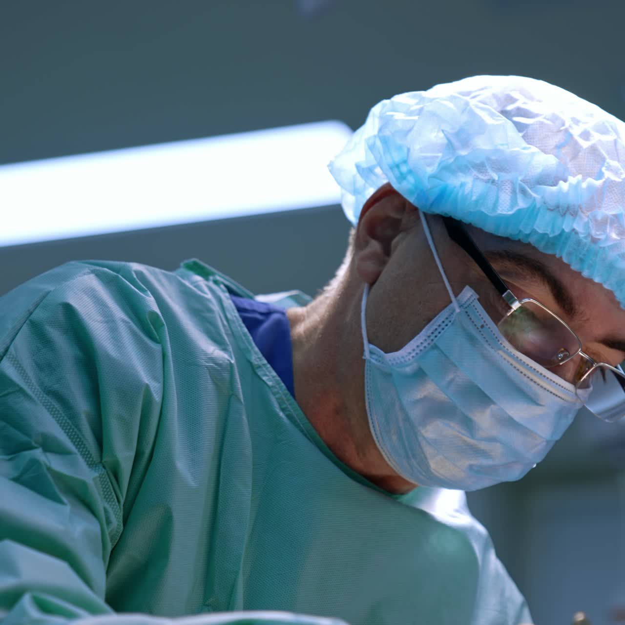 Focused look of an experienced surgeon wearing cap, mask and glasses. Doctor is fully concentrated on operation. Low angle view