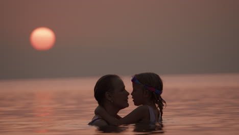 mother and daughter embrace at sunset by the ocean