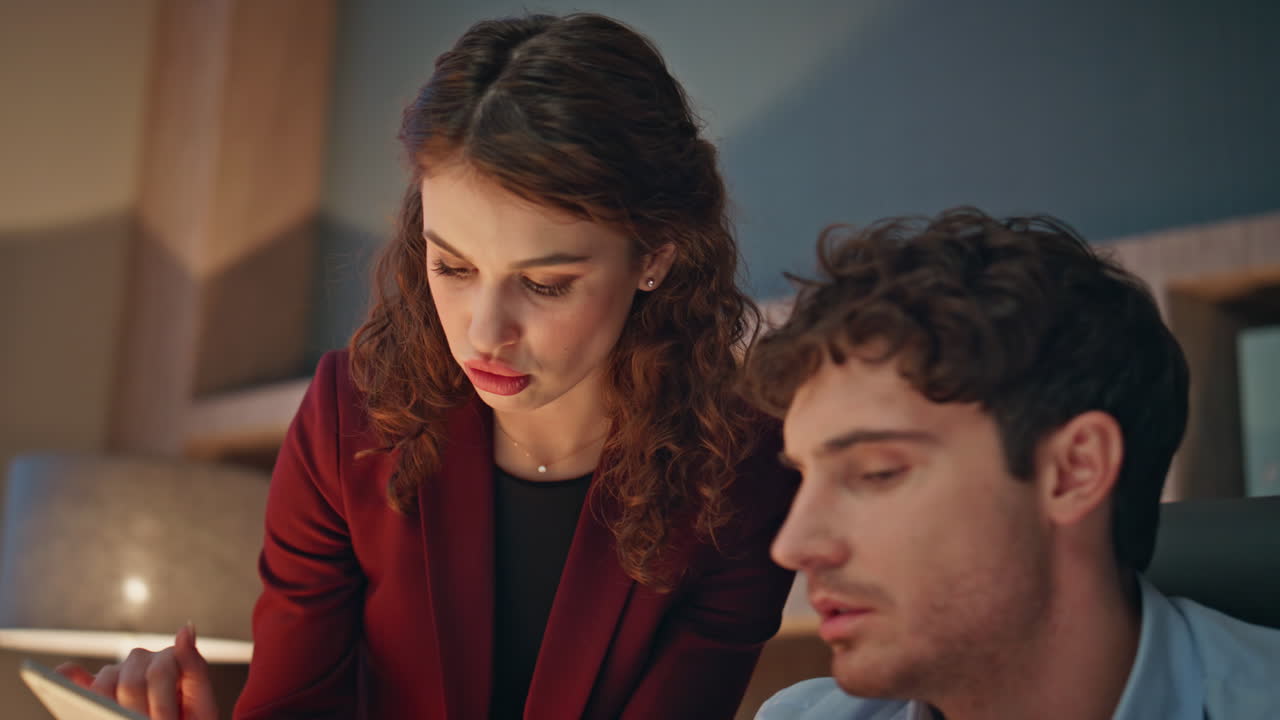 Woman assistant showing tablet data to man employee at evening office close up.