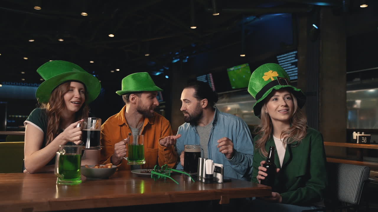 Friends watching a football game on TV in a pub, reacting excited and celebrating victory. Men and women having fun in Irish hats. Saint Patrick's Day.