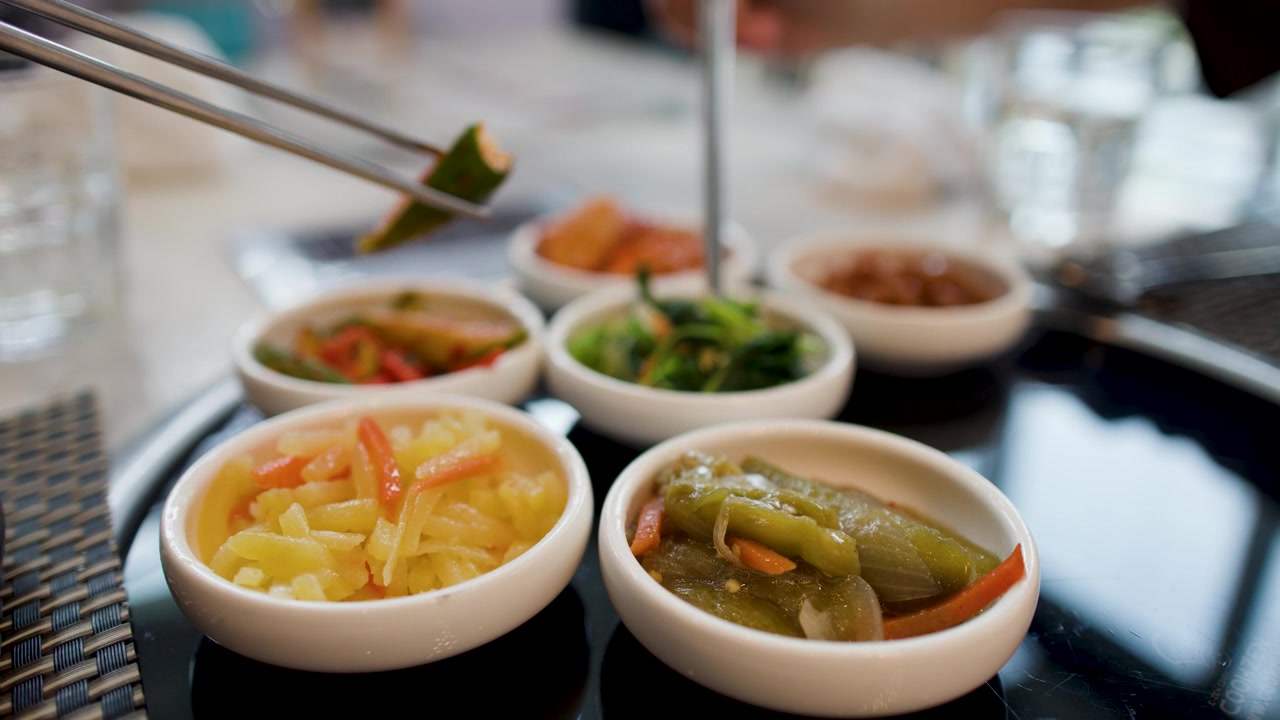 Foto jarak dekat berbagai hidangan pembuka Korea dengan sumpit mengambil bayam di sebuah restoran