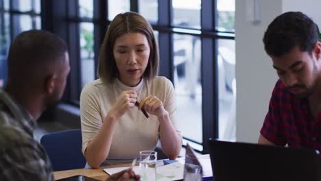 Diverse-business-people-sitting-using-laptop-going-through-paperwork-in-modern-office