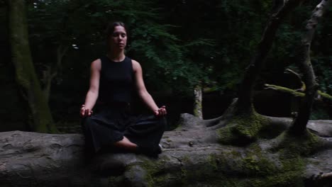 Nature-therapy---young-woman-sitting-in-Sukhasana-on-log