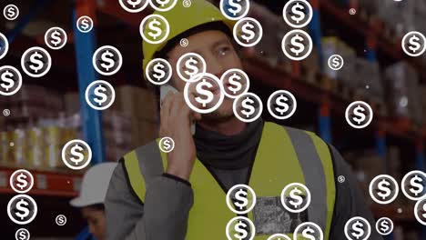 Animation-of-multiple-dollar-symbols-over-caucasian-male-worker-talking-on-smartphone-at-warehouse