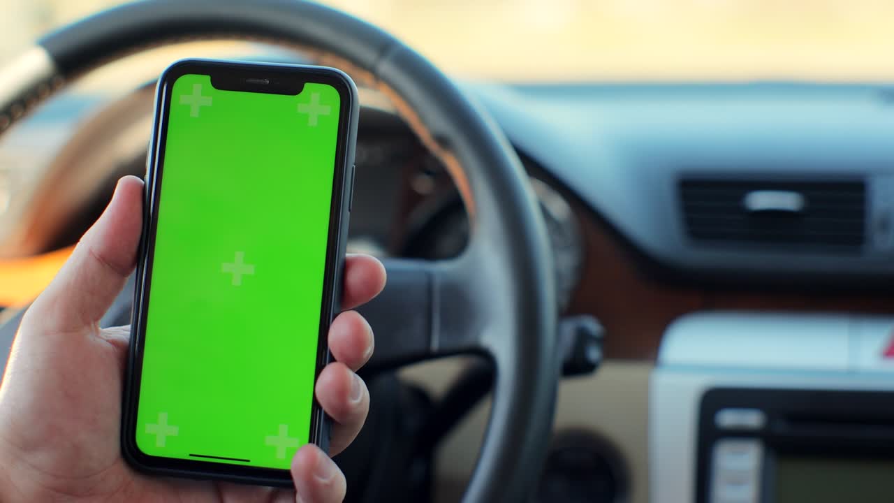 vista de la mano del hombre sosteniendo el teléfono inteligente de pantalla verde en el coche. maqueta de pantalla táctil. búsqueda en internet.
