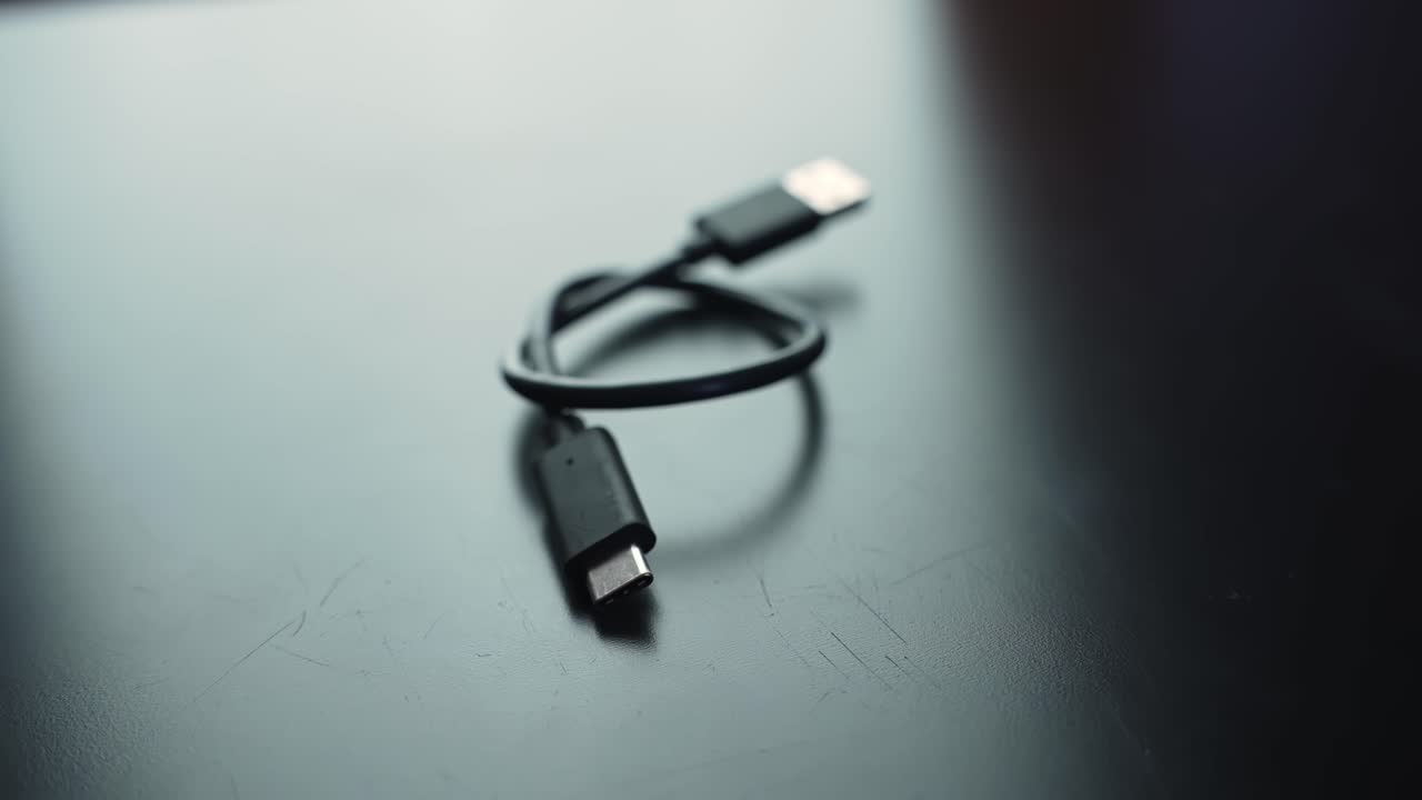 Macro close-up of a USB-C charging cable on a dark desk with shallow depth of field and copy space, perfect for tech, office, and connectivity b-roll