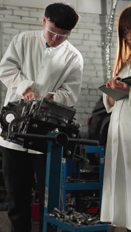 profesional en taller de automóviles mide el grosor del motor utilizando una pinza de vernier mientras el colega registra los datos en la tableta, las características de fondo herramientas mecánicas, coche negro estacionado