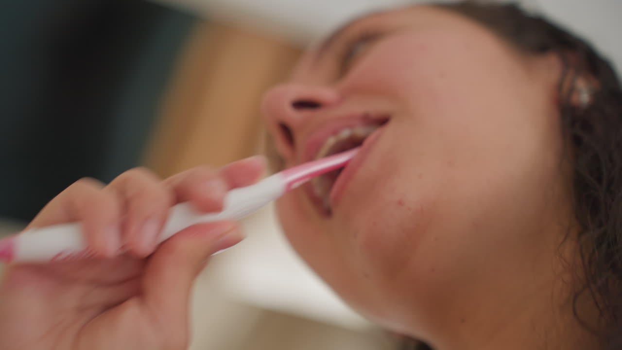 Woman brushing teeth hotel sink closeup, business traveler prepping for day with brisk strokes, lowangle profile and bright hotel lighting, foam and motion convey candid morning energy