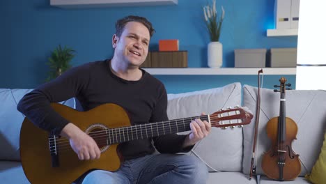 Happy-musician-man-playing-his-guitar-at-home-smiling-happily,-enjoying-his-violin.