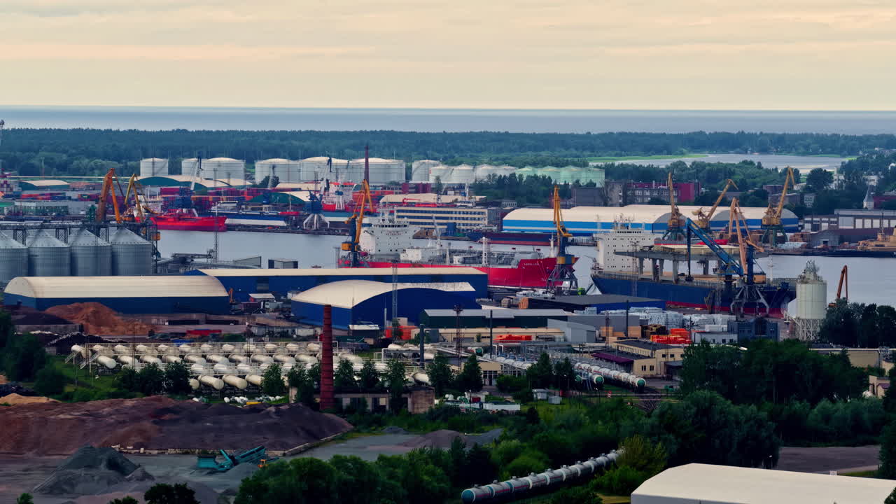 Wide view over an industrial zone featuring cranes, silos, and large halls under clear skies