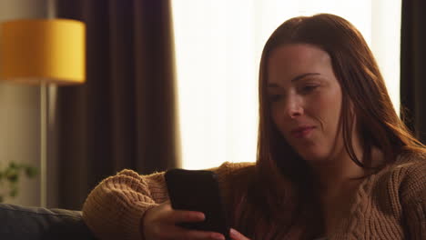 close up of woman sitting on sofa at home using mobile phone to check social media message and scrolling online 2