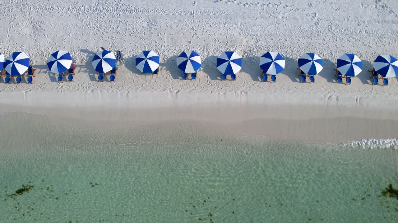 vista aérea de drones de paraguas azules y blancas en una playa de arena blanca con aguas claras en un día soleado