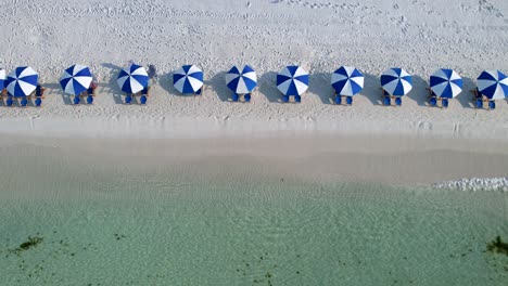 vista aérea de drones de paraguas azules y blancas en una playa de arena blanca con aguas claras en un día soleado