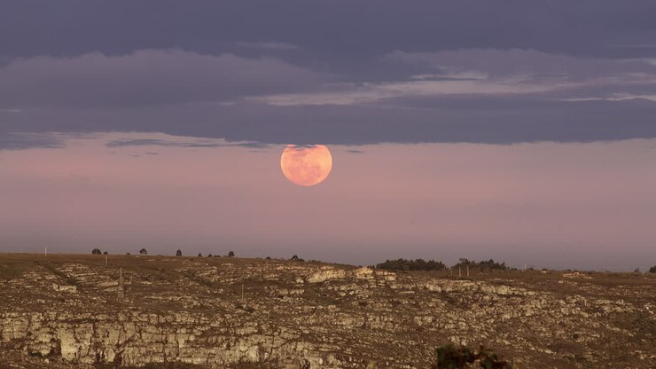 Ascensão de uma lua cheia vermelha e brilhante com nuvens acima do horizonte da Terra.