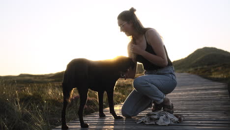 Video-En-Cámara-Lenta-De-Una-Mujer-Joven-Y-Su-Perro-Interactuando-Amándose-Mientras-Se-Pone-El-Sol