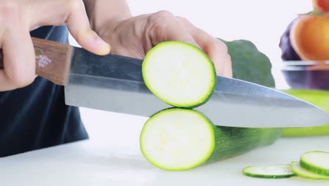 4k mujeres cortando a mano calabacín fresco en la tabla de cortar. la mano femenina corta el pepino japonés crudo en círculos con un cuchillo en la tablilla de cortar, concepto de alimentos saludables.