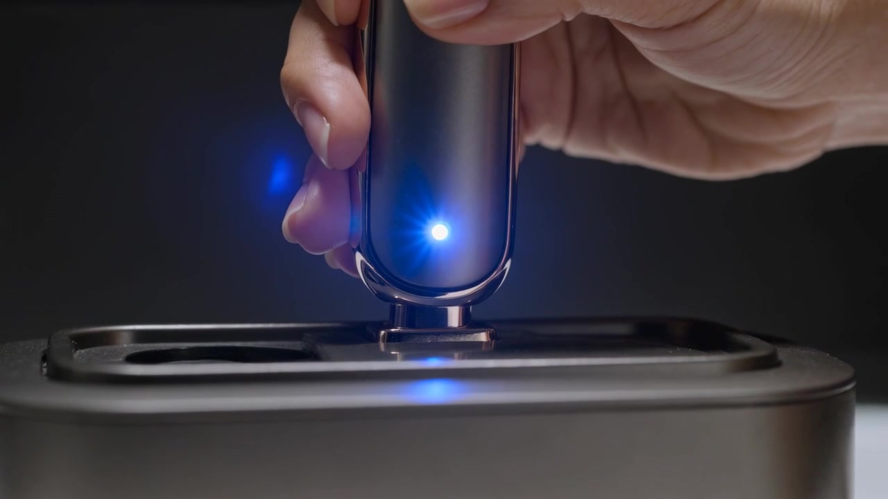Starting docking, right hand lowering metal device into dock on table for charging, LED glowing