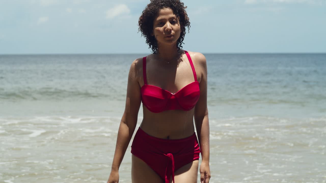 La bellezza di una giornata di sole su una spiaggia di un'isola tropicale è catturata da una giovane ragazza con i capelli ricci in un vistoso bikini rosso che cammina sulla spiaggia.