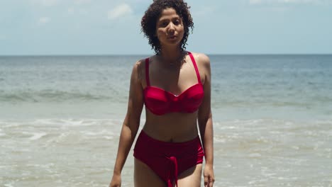 the beauty of a sunny day on a tropical island beach is captured by a young girl with curly hair in a striking red bikini walking on the beach